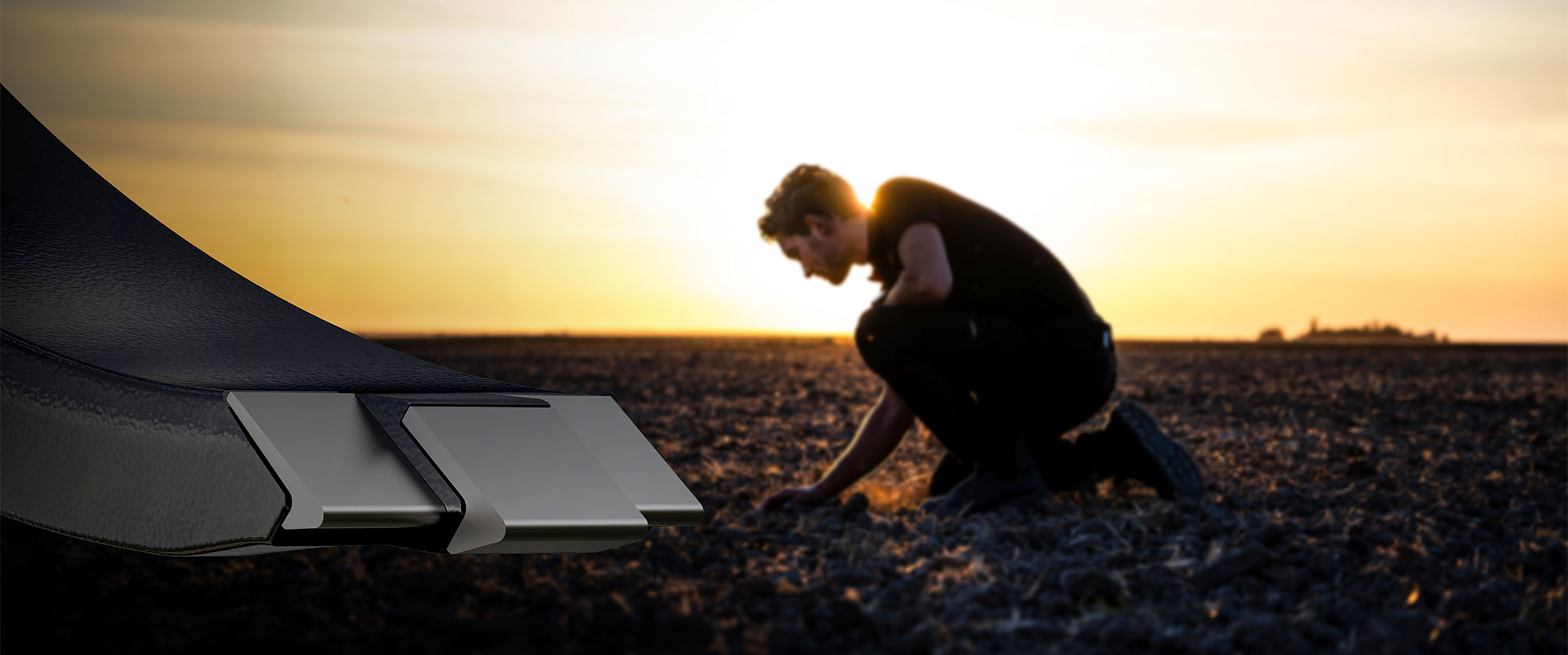 Man crouching in a plowed field, hand in the soil. The sun is rising in the background.